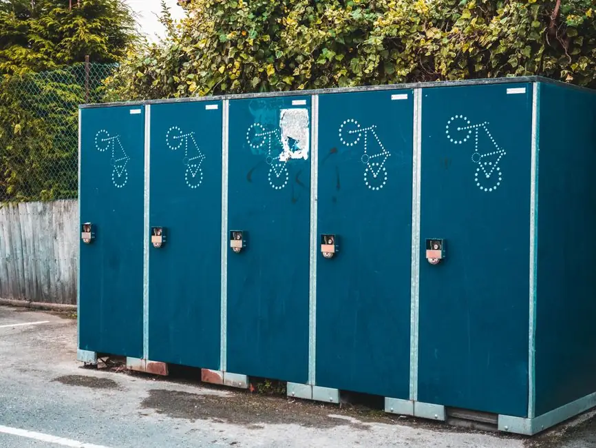 Outdoor blue portable toilet containers aligned in a row against a leafy backdrop.
